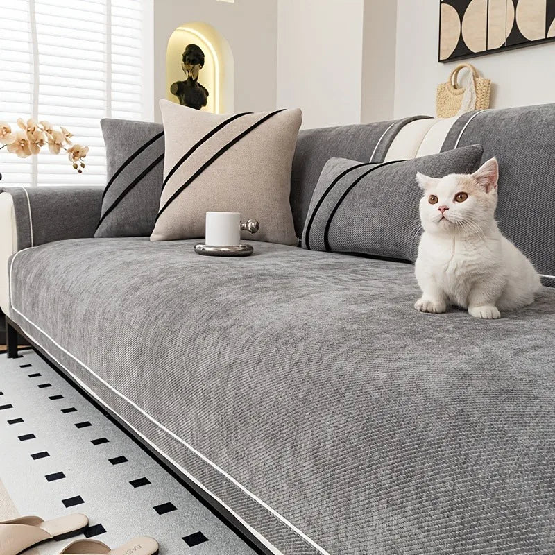 Katt sitter på ett silvergrått soffskydd i chenille